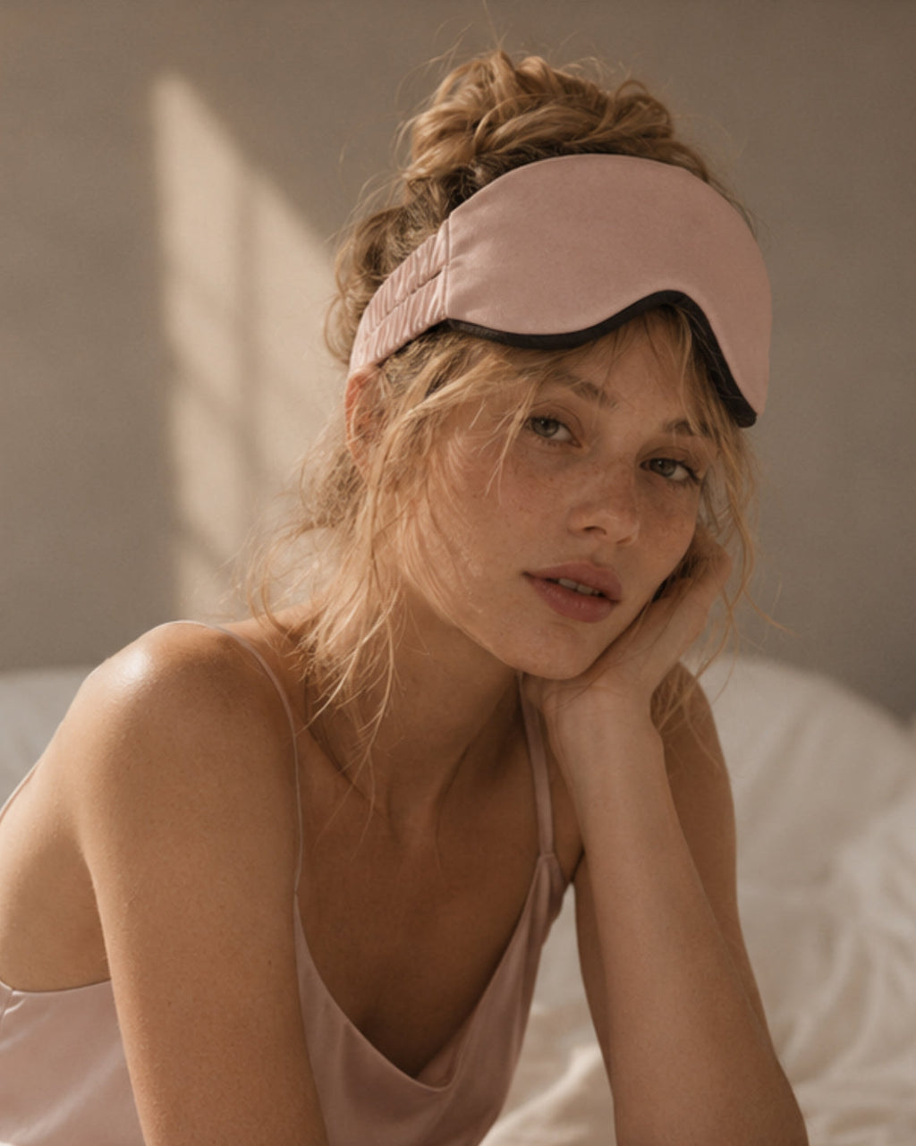 Woman resting in soft morning light wearing the Driftnest weighted sleep mask pushed up on her forehead