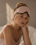 Woman resting in soft morning light wearing the Driftnest weighted sleep mask pushed up on her forehead