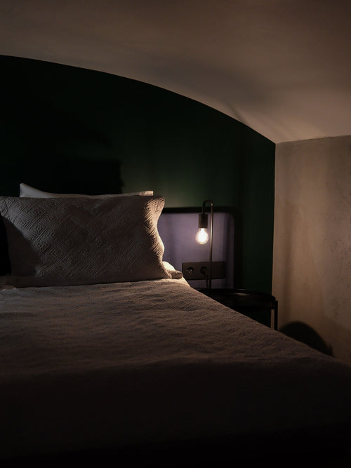 A dim, quiet bedroom at night with a single warm lamp — the calm the Driftnest White Noise Machine helps create