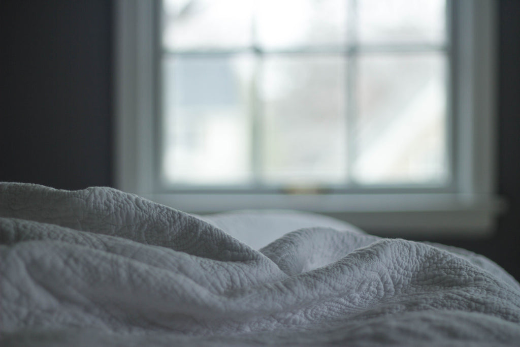 Soft quilted bedding lit by morning window light, the calm, restful atmosphere the Driftnest mask is designed for