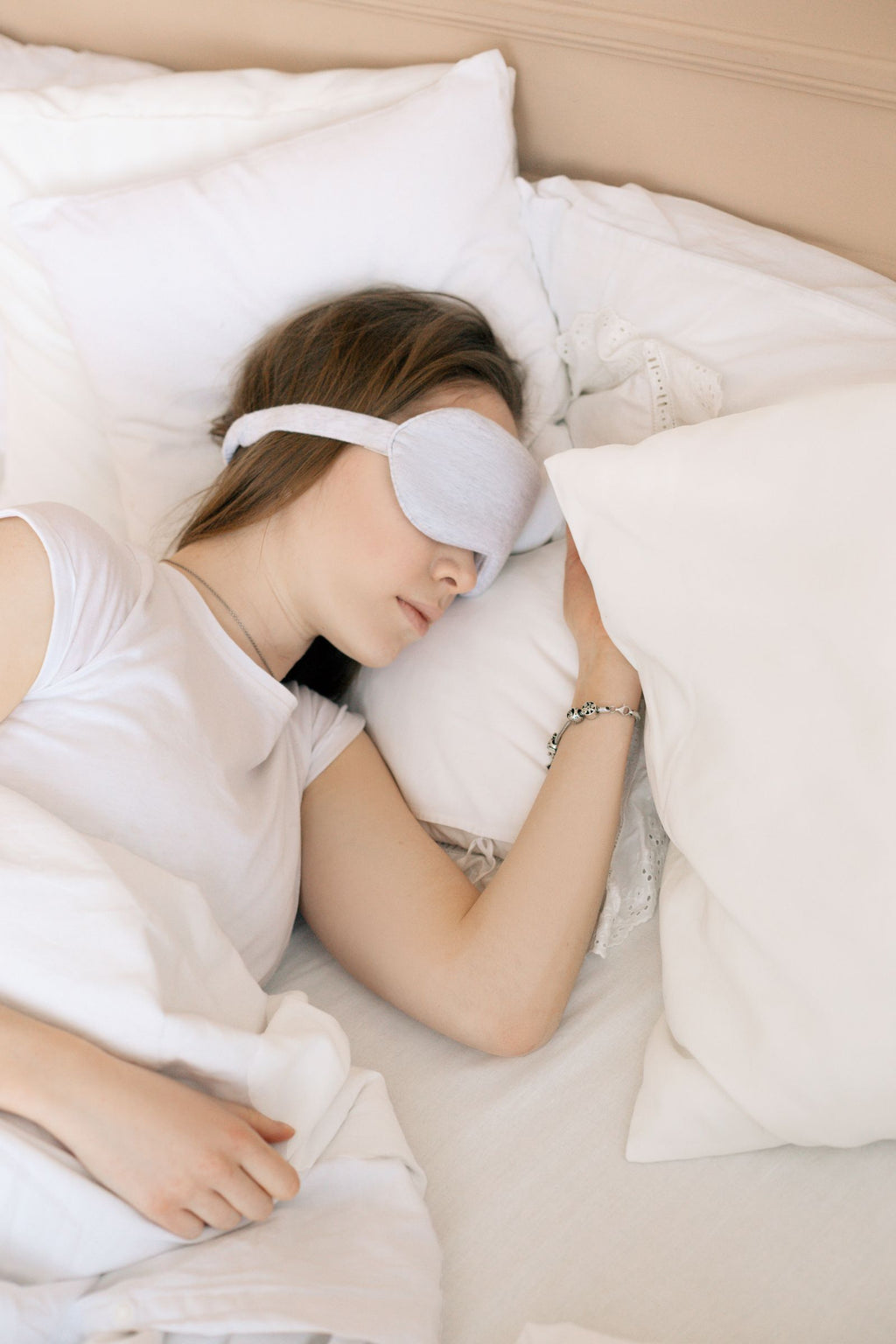 A person asleep wearing a soft eye mask in a calm, neutral-toned bedroom