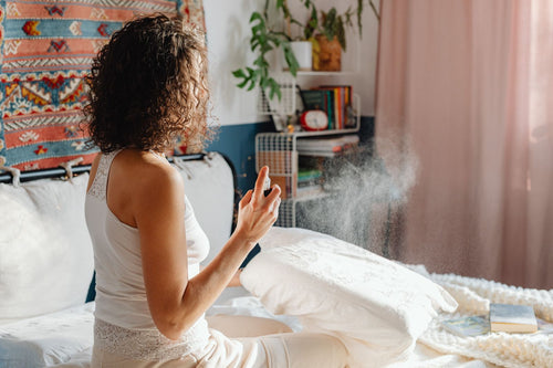 TEMPORARY placeholder lifestyle photo (licensed stock, to be replaced with real product photography): a woman misting her pillow as part of a calming bedtime routine